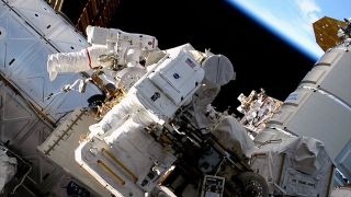 two astronauts in spacesuits on the outside of a space station with Earth in the background