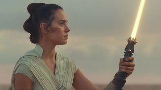 Still from a Star Wars movie. Here we see a close up of Rey holding up a yellow lightsaber while she stares at it intently.