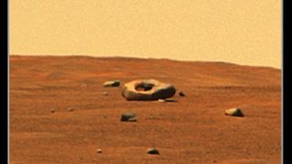 large black rock with a hole in its center sitting on mars&#039; reddish-brown surface