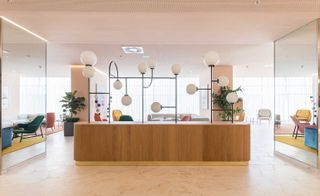 A hotel sitting area with, a variety of different colour chairs, mirrors and a wooden counter with artistically shaped lights on.