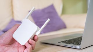 A person holding a Wi-Fi extender next to a laptop