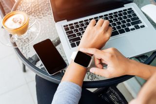 An Apple Watch, an iPhone and a MacBook in a cafe.