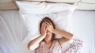 Young woman lies in bed with sleep problems caused by choosing a memory foam hybrid instead of a latex hybrid