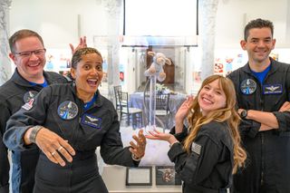 people in blue flight suits smile and pose for a picture in front of a rocket