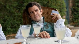 Benedict Bridgerton holds playing cards with lemonade in front of him 