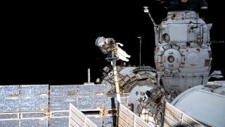 an astronaut in spacesuit floating near the international space station. visible near him are solar panels and several modules