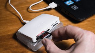 Hand putting SD card into a card reader attached to a laptop on a desk