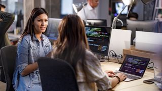 A female programmer communicating with her colleague while both work on code in an office.