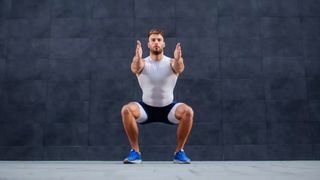 Man performing a squat face on against a grey background outside