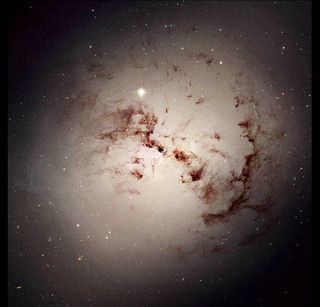 An elliptical galaxy, full of dark lanes of gas, likely formed in the merger of two other galaxies. Elliptical galaxies host less (or no) star birth than spiral galaxies like the Milky Way.