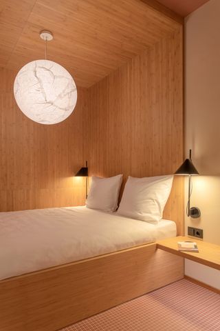A wooden bedroom with bed and Noguchi-style lamp