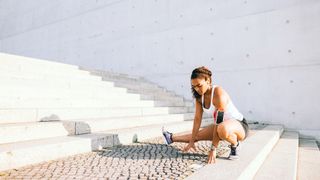 Woman performing a Cossack squat outdoors next to steps with left leg bent and right leg extended