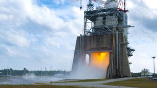 fire and smoke billow out of an industrial-looking rocket engine testing facility