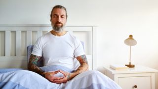 Man with tattoos sits upright in bed
