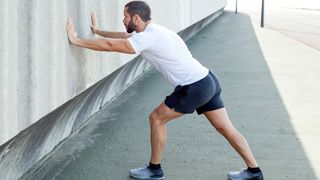 Man with arms pressed on a wall left leg forward and right leg back