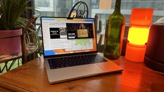 A 2023 14-inch MacBook Pro on a wooden counter, near a retro lamp.