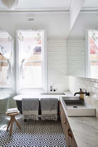 The bathrooms with geometric black and white tiles, bath tub and towels.