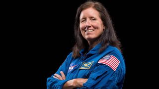 Photo of NASA astronaut Shannon Walker in a blue flight suit with American flag patch on the sleeves. She is crossing her arms and smiling at the camera.