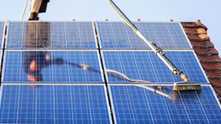 Solar panels on roof being cleaned with a long-handled brush