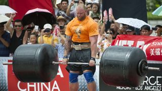 A very large man deadlifts a barbell with huge weights on either side