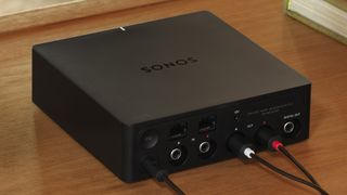 A black Sonos Port on a wooden table, with three cables plugged into it.