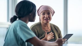 A cancer patient and her doctor sitting at a table as they go over information on a tablet.