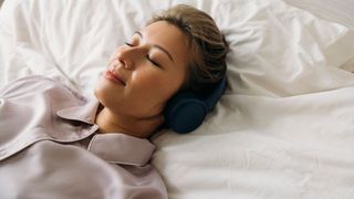 A smiling woman with headphones lies in bed listening to a bedtime story for adults