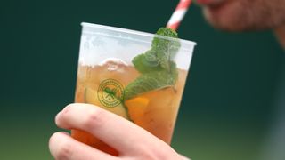 A close up of a someone drinking a Wimbledon branded cup of Pimms at Wimbledon 2024.