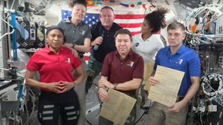 Six people in the low gravity environment of the international space station, positioned with three in front and three in the back.