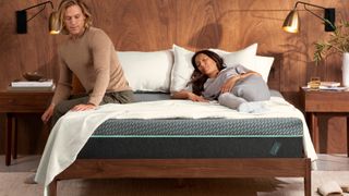 A man sits on the edge of the Tuft & Needle Mint Hybrid mattress while a woman sleeps on the other side