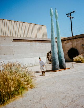 Sterling Ruby standing outside studio next to metal sculpture