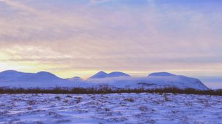 abisko national park with mountains in the background and snow in the foreground. The sky is yellow, orange and slightly blue while the snow on the ground appears blue.