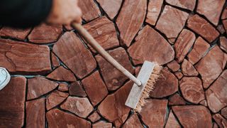 Someone using a broom to sweep patio stones