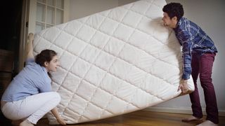 A man and a woman move a mattress