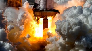 ground-level view of flames and exhaust billowing from a silver rocket on a test stand