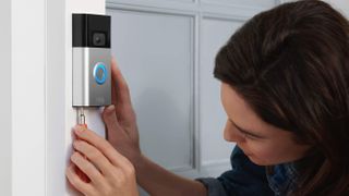 A woman installing a Ring camera against a white wall