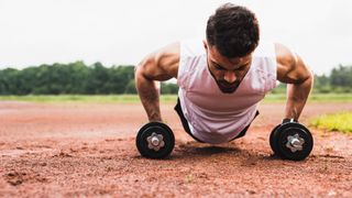 Man performing a burpee holding two dumbbells during outdoor workout