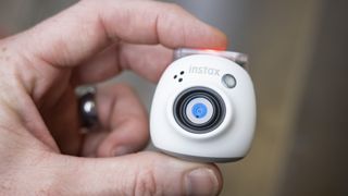 White Fujifilm Instax Pal in the hand with sidewalk background