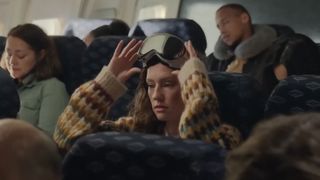 A woman wearing the Apple Vision Pro while on a plane with other passengers next to them.