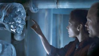 a woman reaches out to touch a floating column of water shaped like a human face