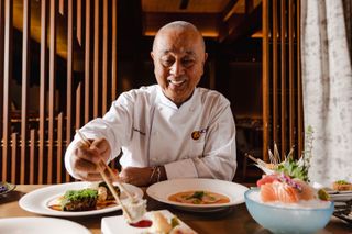 Chef Nobuyuki ‘Nobu’ Matsuhisa eating food with chopsticks and smiliing