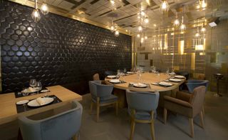 A dining area with decorated tables, chairs, pendant lights and patterned walls and ceilings.