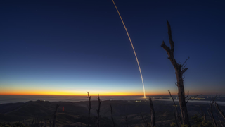 a rocket launches at night, leaving a streak of light through the sky