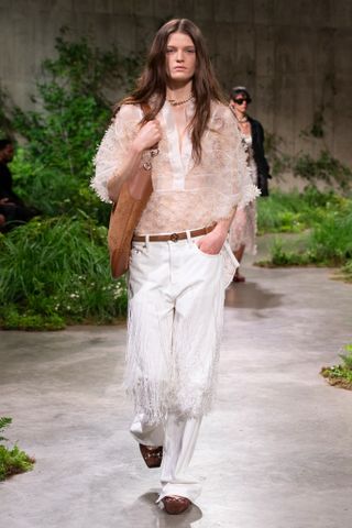 Model in floral adorned blouse and white jeans wals the Gucci Cruise 2025 runway show