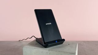 The Anker 313 Charger Stand is angled slightly to the right. It's sitting on a cement block against a pink background.