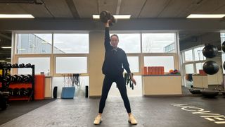 Writer Sam performing a dumbbell snatch in a gym using the Bowflex SelectTech 552i adjustable dumbbell raised in the air overhead with right arm raised