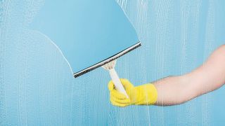 Someone cleaning glass with a squeegee while wearing rubber gloves