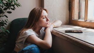 A photograph of a woman looking sad and gazing out a window.