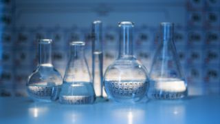 Beakers in front of the periodic table.