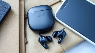 Bose QuietComfort Earbuds 2 er placeret ved siden af etuiet og en telefon